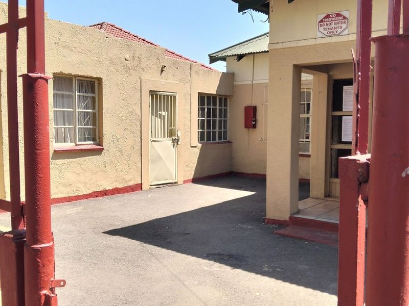 Front entrance area featuring a paved driveway, metal security gate, and security-barred windows on a stucco-finished building exterior.