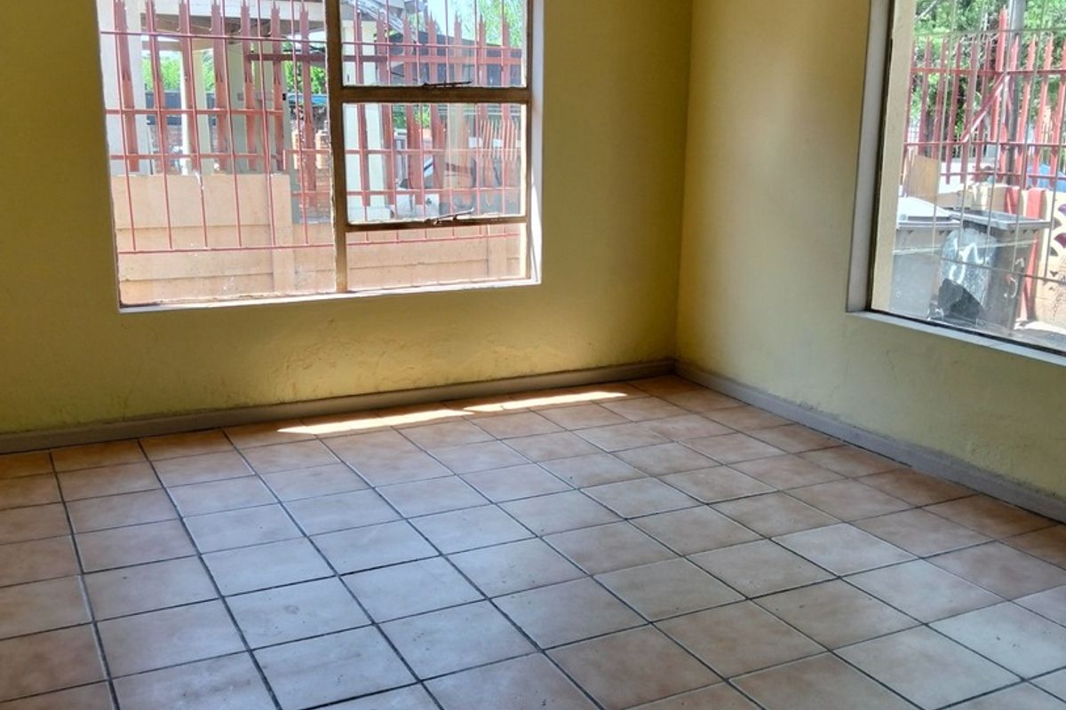 An empty living room featuring tiled flooring and large windows with security bars, offering a blank canvas for potential renovation.