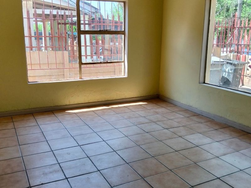 An empty living room featuring tiled flooring and large windows with security bars, offering a blank canvas for potential renovation.