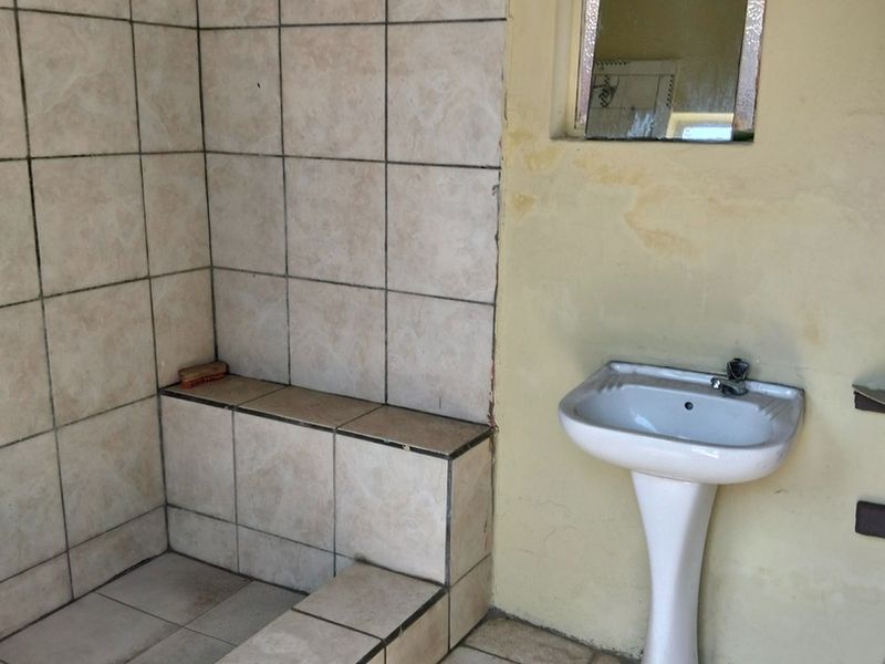 A dated bathroom featuring a tiled shower enclosure and a pedestal basin, requiring cosmetic updates and repairs to the wall finishes and tiling.