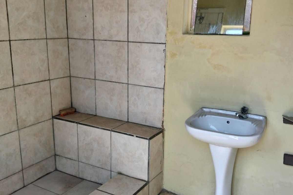 A dated bathroom featuring a tiled shower enclosure and a pedestal basin, requiring cosmetic updates and repairs to the wall finishes and tiling.
