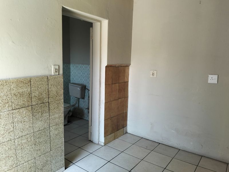 A vacant hallway area featuring tiled flooring and wall tiling, leading into a bathroom space with dated finishes.
