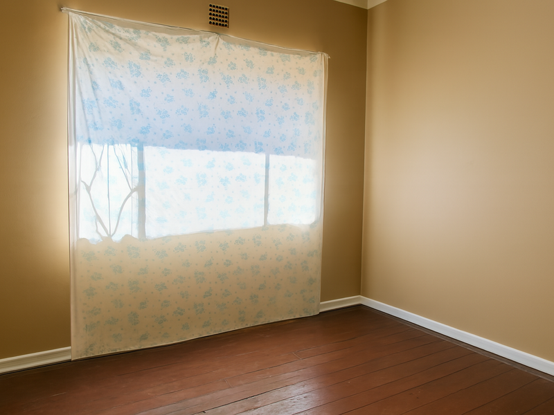 An empty bedroom featuring timber flooring, neutral wall paint, and a ventilation grille above the window area.
