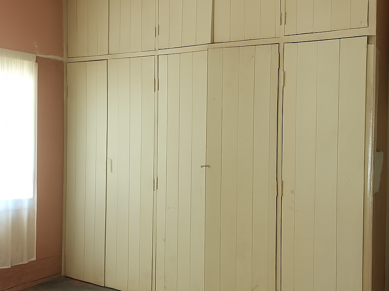A bedroom featuring extensive built-in floor-to-ceiling timber cabinetry and original timber flooring, offering ample storage space in a classic layout.