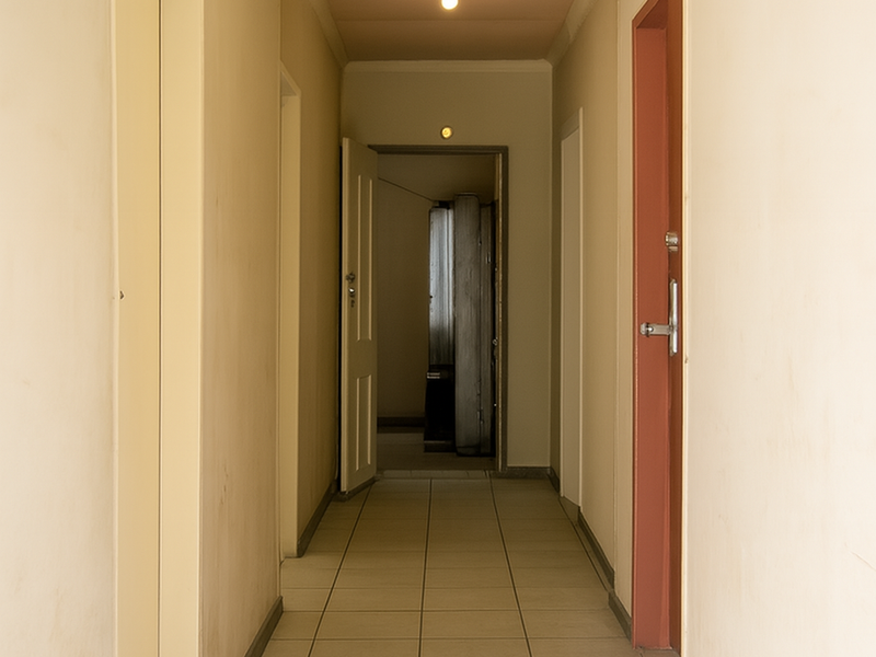 A long, empty residential hallway featuring tiled flooring and multiple internal doors, requiring cosmetic updates to improve the overall aesthetic.