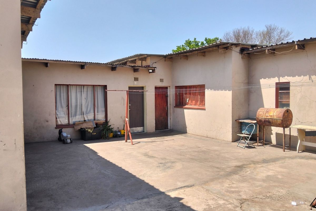 Rear exterior view of the property featuring a concrete courtyard, metal roofing, and access doors to the main building structure.