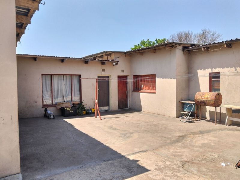 Rear exterior view of the property featuring a concrete courtyard, metal roofing, and access doors to the main building structure.