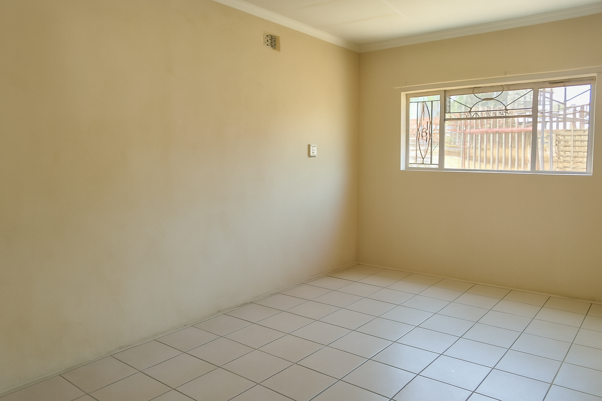 A vacant bedroom featuring neutral tiled flooring, plain walls, and a window fitted with security bars.
