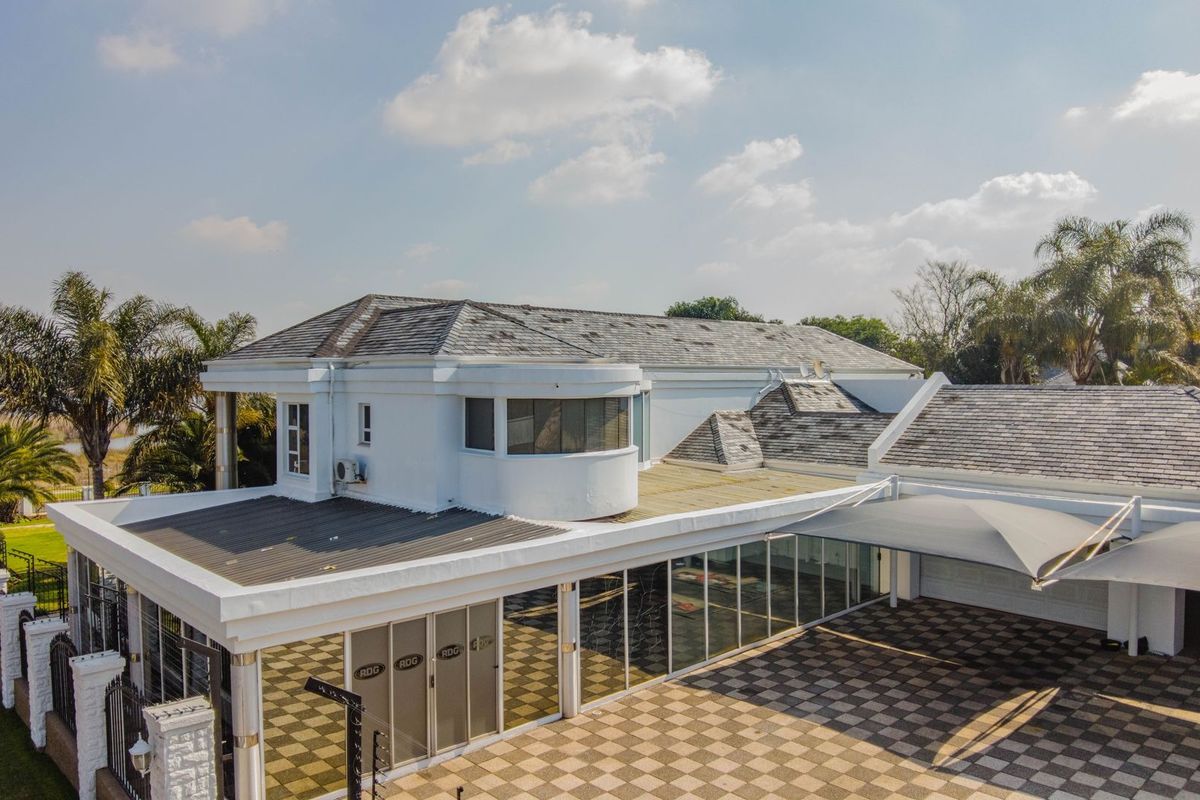 Aerial view of a large residential property featuring a tiled roof, extensive paved driveway, and covered outdoor parking area.