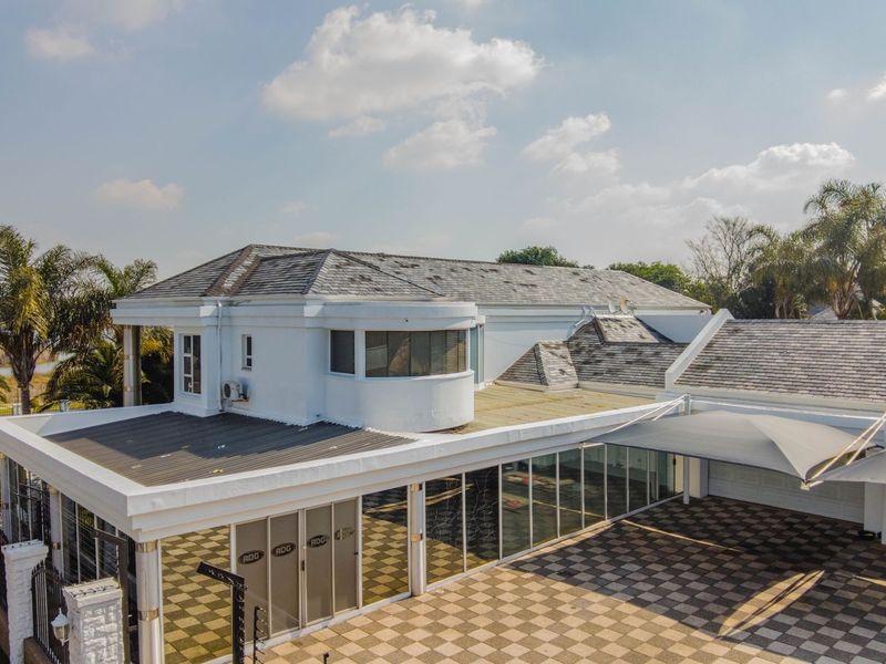 Aerial view of a large residential property featuring a tiled roof, extensive paved driveway, and covered outdoor parking area.