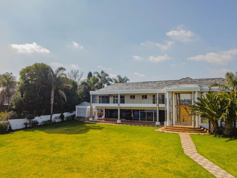 Spacious rear exterior view of a large two-story residence featuring a manicured lawn, stone walkway, and a covered balcony.