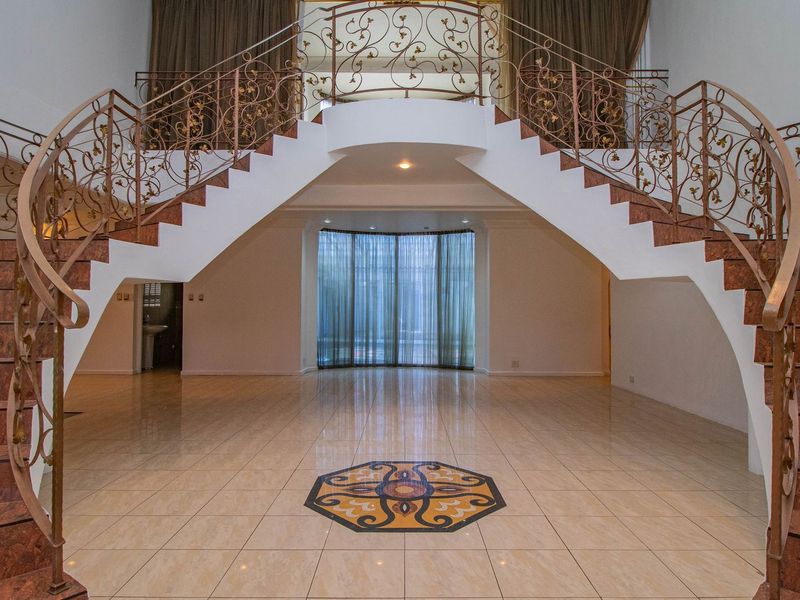 Grand entrance hall featuring a symmetrical dual staircase with ornate wrought iron railings, polished tile flooring, and a decorative central floor inlay.
