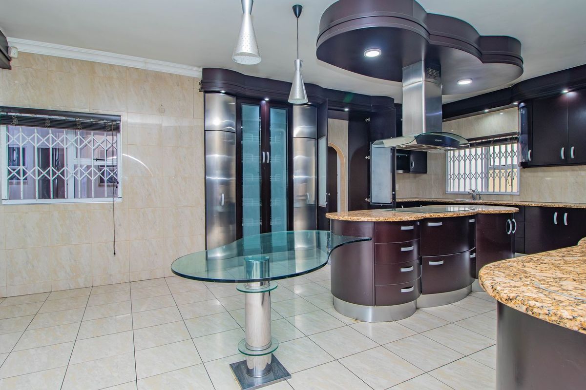 Spacious kitchen featuring dark cabinetry, granite countertops, a central island with a glass breakfast bar, and modern recessed ceiling lighting.