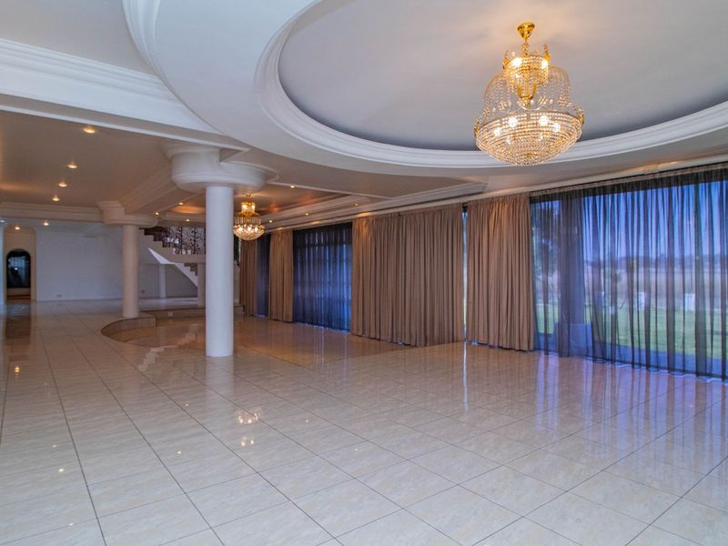 Spacious open-plan living area featuring polished tiled floors, decorative recessed ceilings with crystal chandeliers, and large sliding glass doors leading to the exterior.