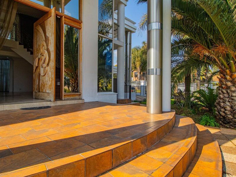 A grand entrance featuring a tiled porch with curved steps, stainless steel columns, and a striking carved wooden front door with large glass panels.