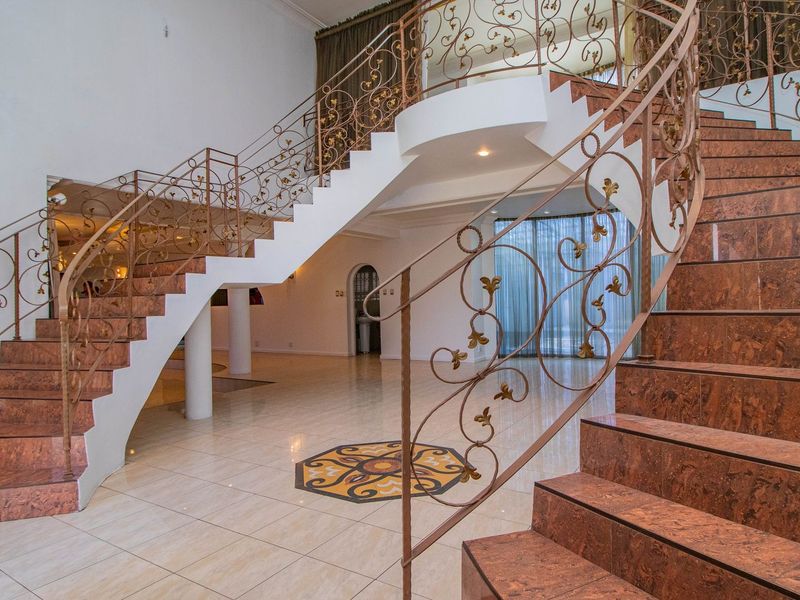 Grand entrance foyer featuring a sweeping staircase with ornate wrought iron balustrades and polished tiled flooring with a decorative central inlay.