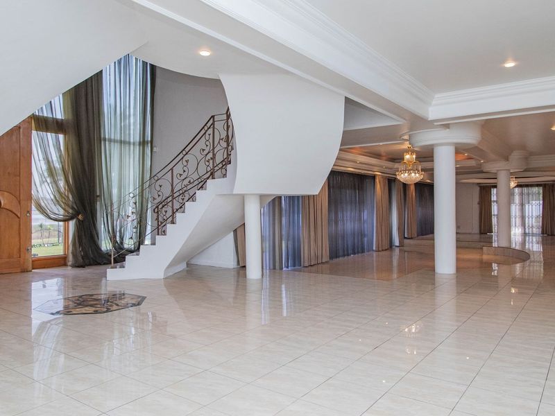 A spacious, open-plan living area featuring polished tile floors, a grand staircase with wrought iron detailing, and elegant structural columns.