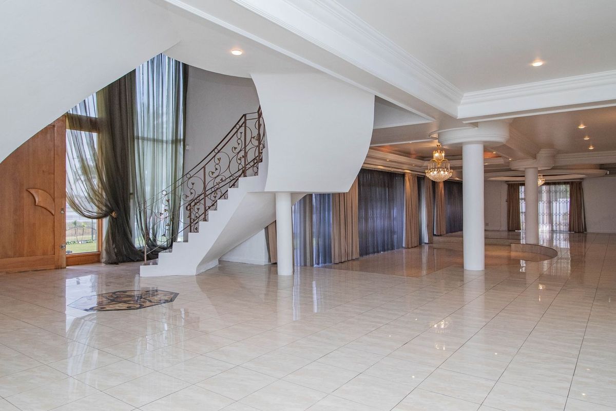 A spacious, open-plan living area featuring polished tile floors, a grand staircase with wrought iron detailing, and elegant structural columns.