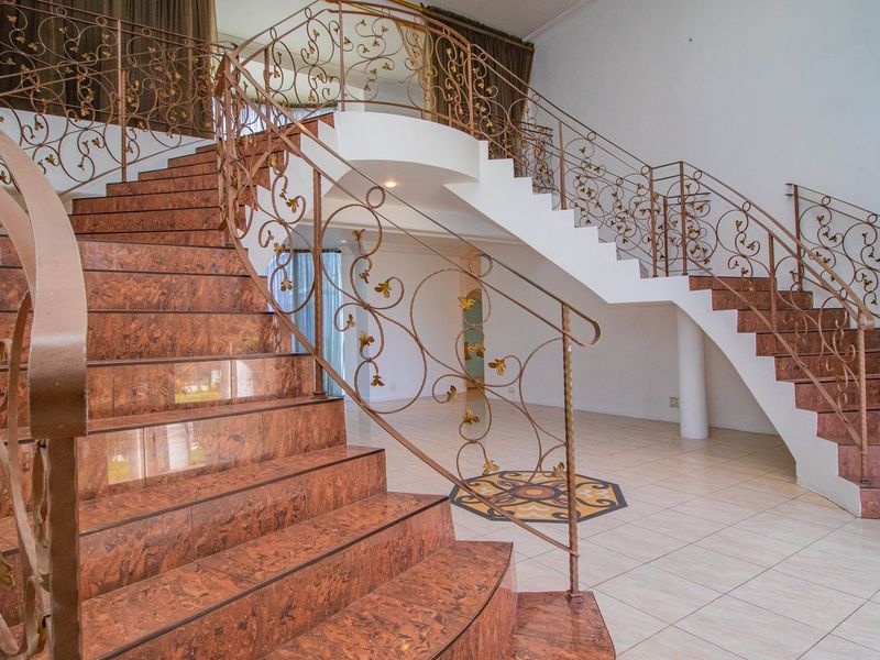 Grand entrance foyer featuring a sweeping curved staircase with ornate wrought iron balustrades and polished marble treads, leading to an open-plan living area.