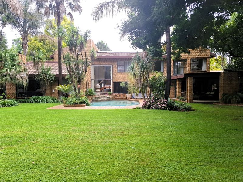 Spacious rear garden featuring a swimming pool, established landscaping, and a brick-faced residence with a covered patio area.