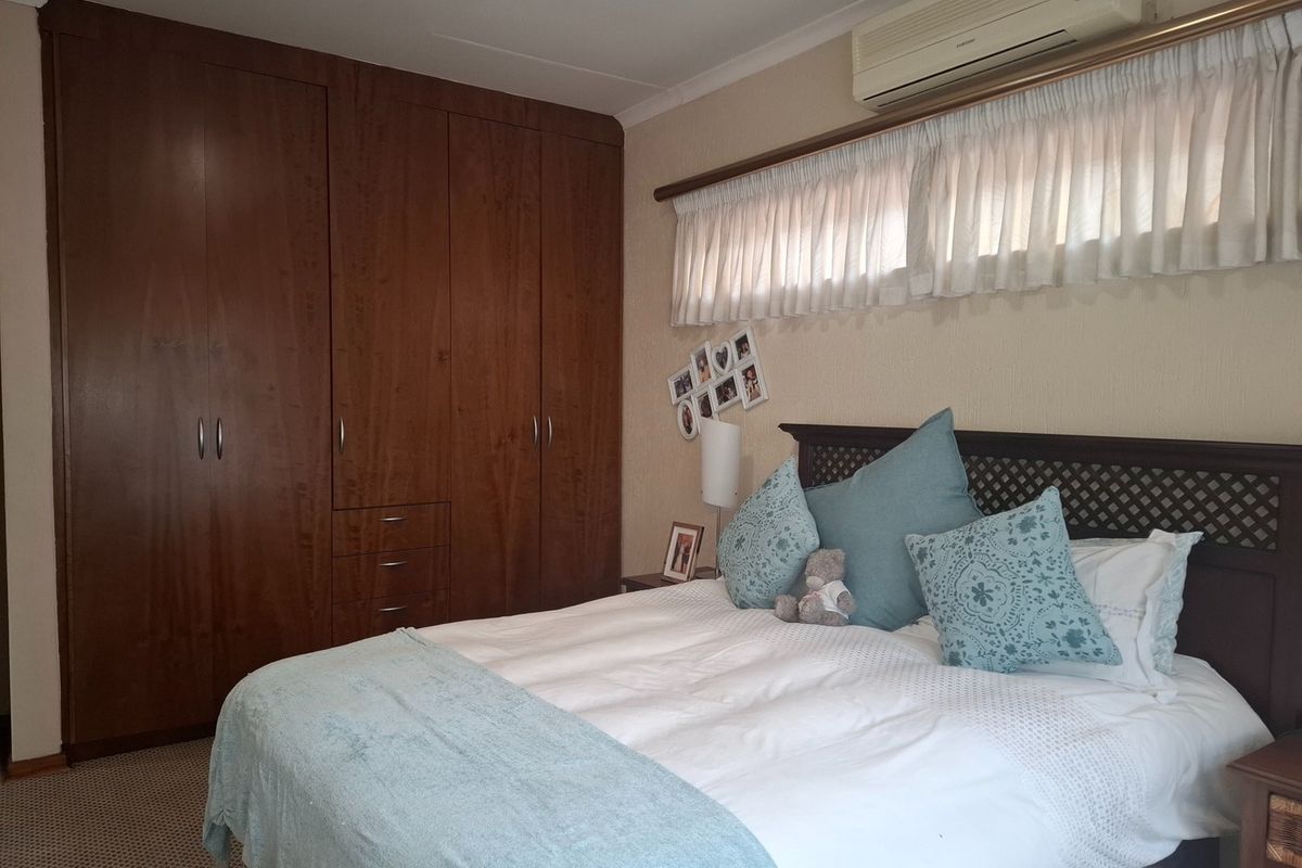 A bedroom featuring built-in wooden cupboards, carpeted flooring, and a wall-mounted split-system air conditioning unit.