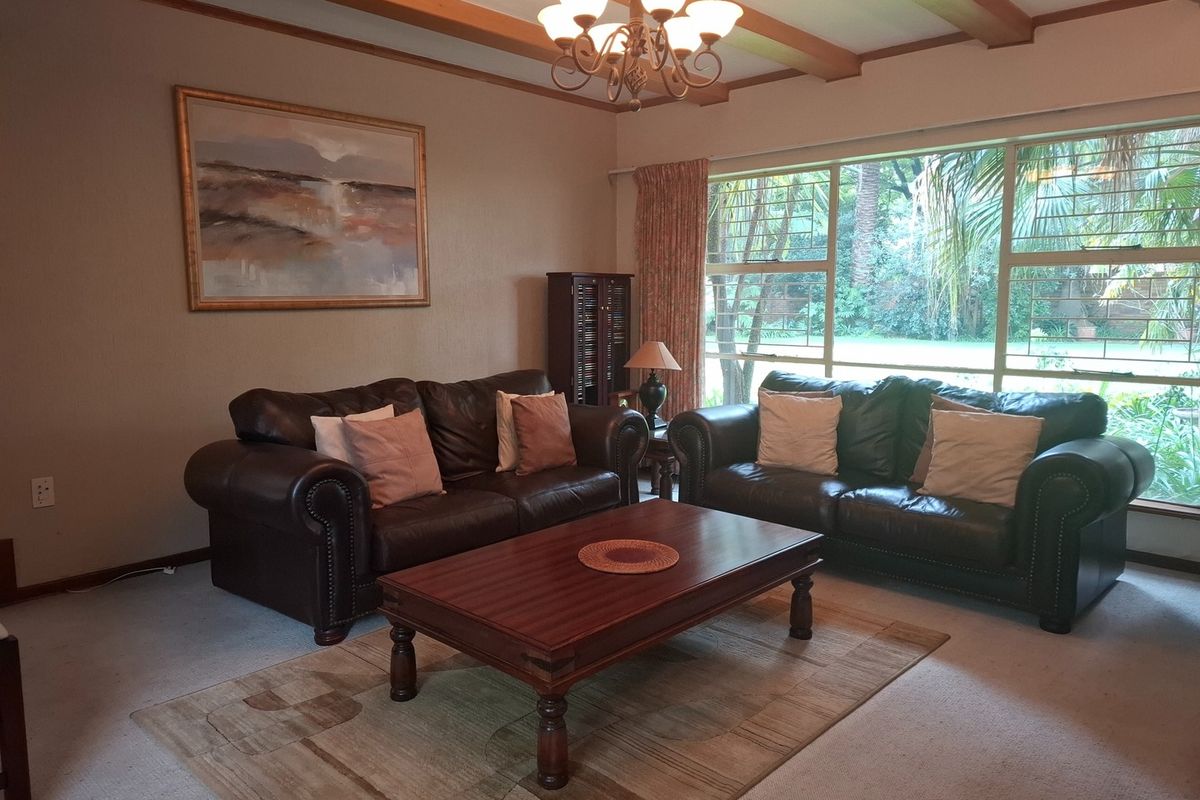 A comfortable living room featuring exposed timber ceiling beams, a large picture window with garden views, and a classic chandelier.