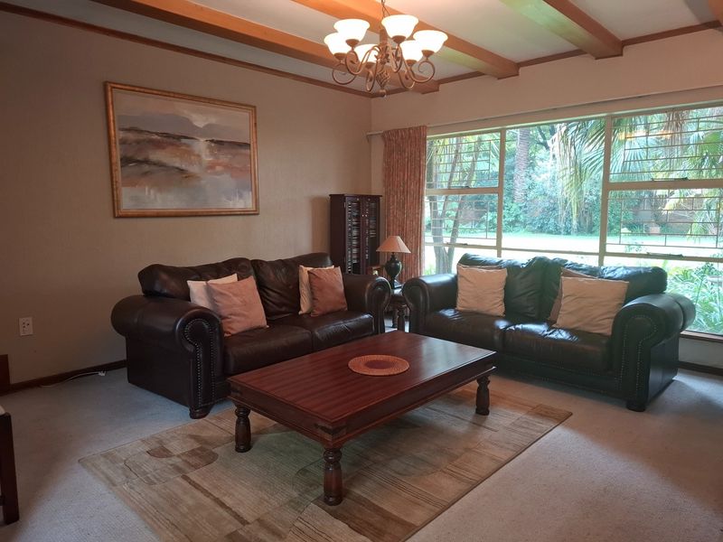 A comfortable living room featuring exposed timber ceiling beams, a large picture window with garden views, and a classic chandelier.