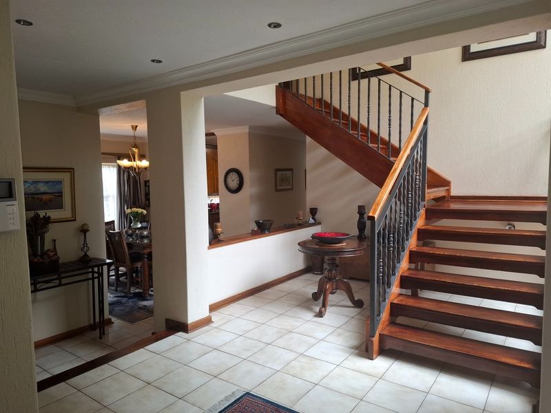 Spacious entrance hall featuring a prominent wooden staircase with wrought iron balustrade, tiled flooring, and open-plan access to the dining area.