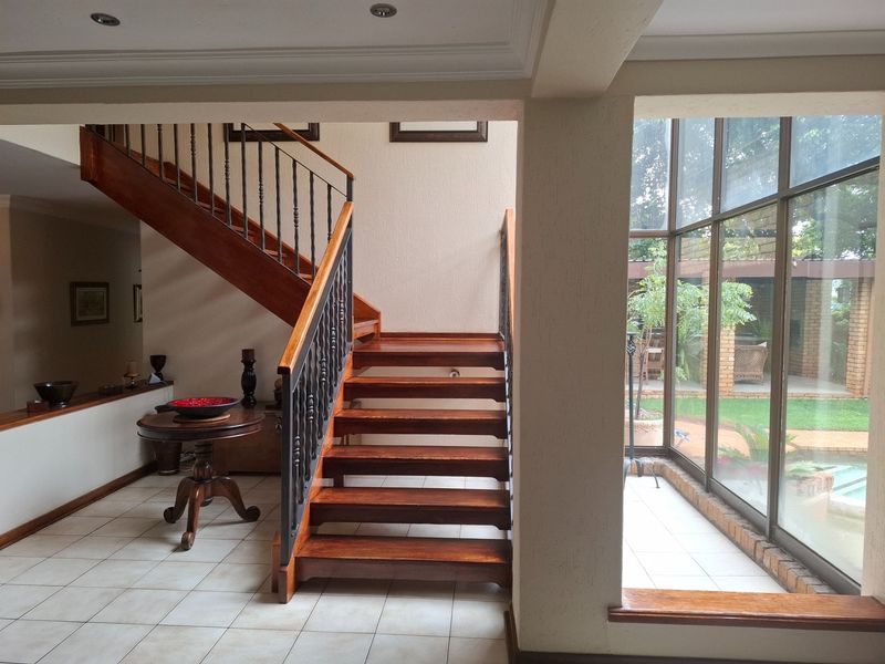 Spacious entrance hall featuring a wooden staircase with wrought iron balustrade, tiled flooring, and large floor-to-ceiling windows overlooking the garden.