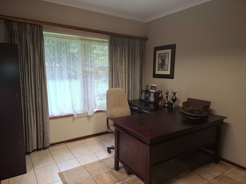 A functional home office space featuring tiled flooring, neutral wall tones, and large windows with fitted curtain rails.
