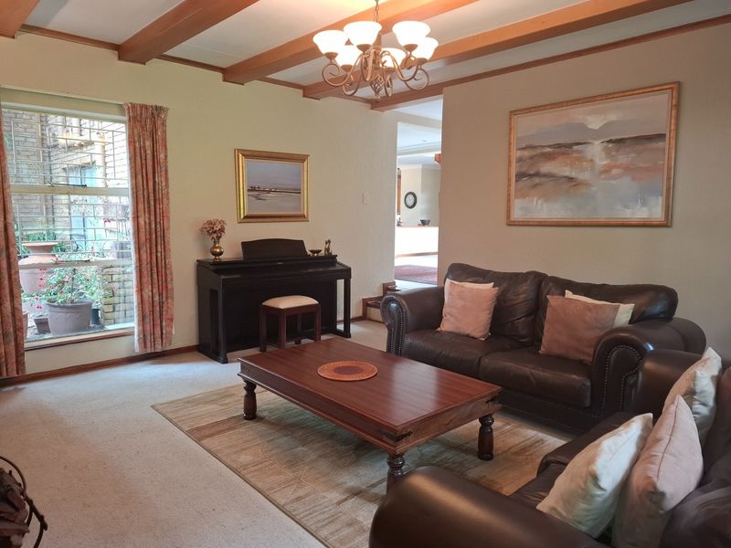 A comfortable living room featuring exposed timber ceiling beams, a central chandelier, and carpeted flooring, offering a warm and traditional atmosphere.