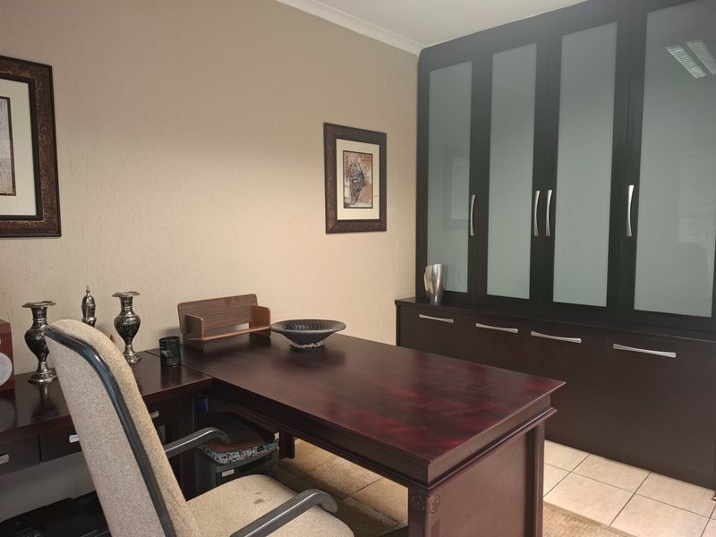 A functional home office featuring built-in dark wood cabinetry with frosted glass inserts and neutral tiled flooring.