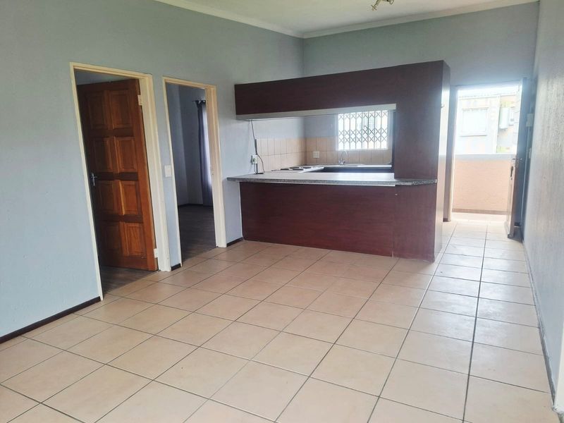 Open plan living area featuring tiled flooring and a functional kitchen with built-in cabinetry and a breakfast bar, leading to an outdoor balcony.