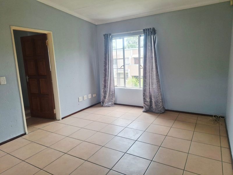 An empty bedroom featuring tiled flooring, a window with security bars, and a timber door, offering a blank canvas for personalization.
