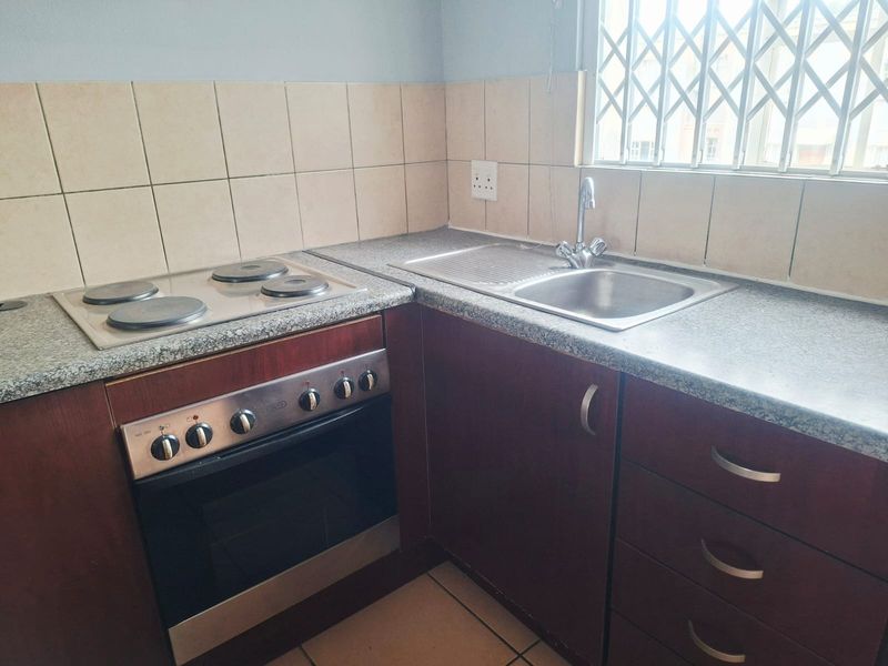 A functional kitchen area featuring dark wood cabinetry, a built-in oven with electric hob, stainless steel sink, and neutral tiled backsplash.