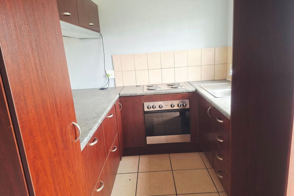 A compact kitchen featuring dark wood-finish cabinetry, granite-look laminate countertops, a built-in oven with electric hob, and neutral ceramic floor tiles.