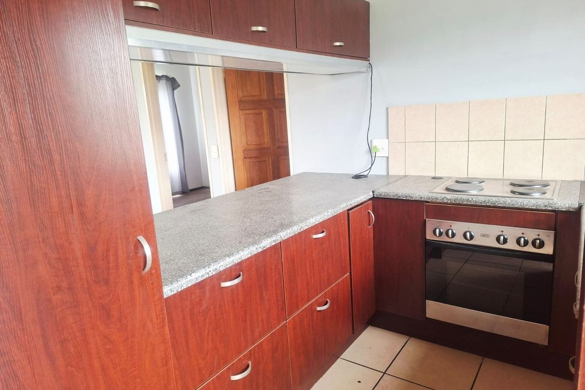A functional kitchen featuring dark wood-look cabinetry, granite-style countertops, a built-in oven with electric hob, and tiled flooring.