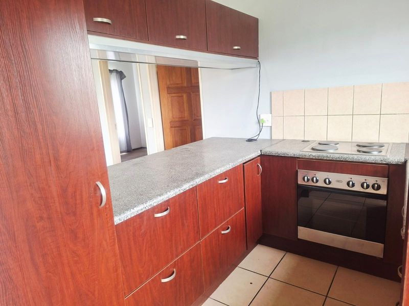A functional kitchen featuring dark wood-look cabinetry, granite-style countertops, a built-in oven with electric hob, and tiled flooring.