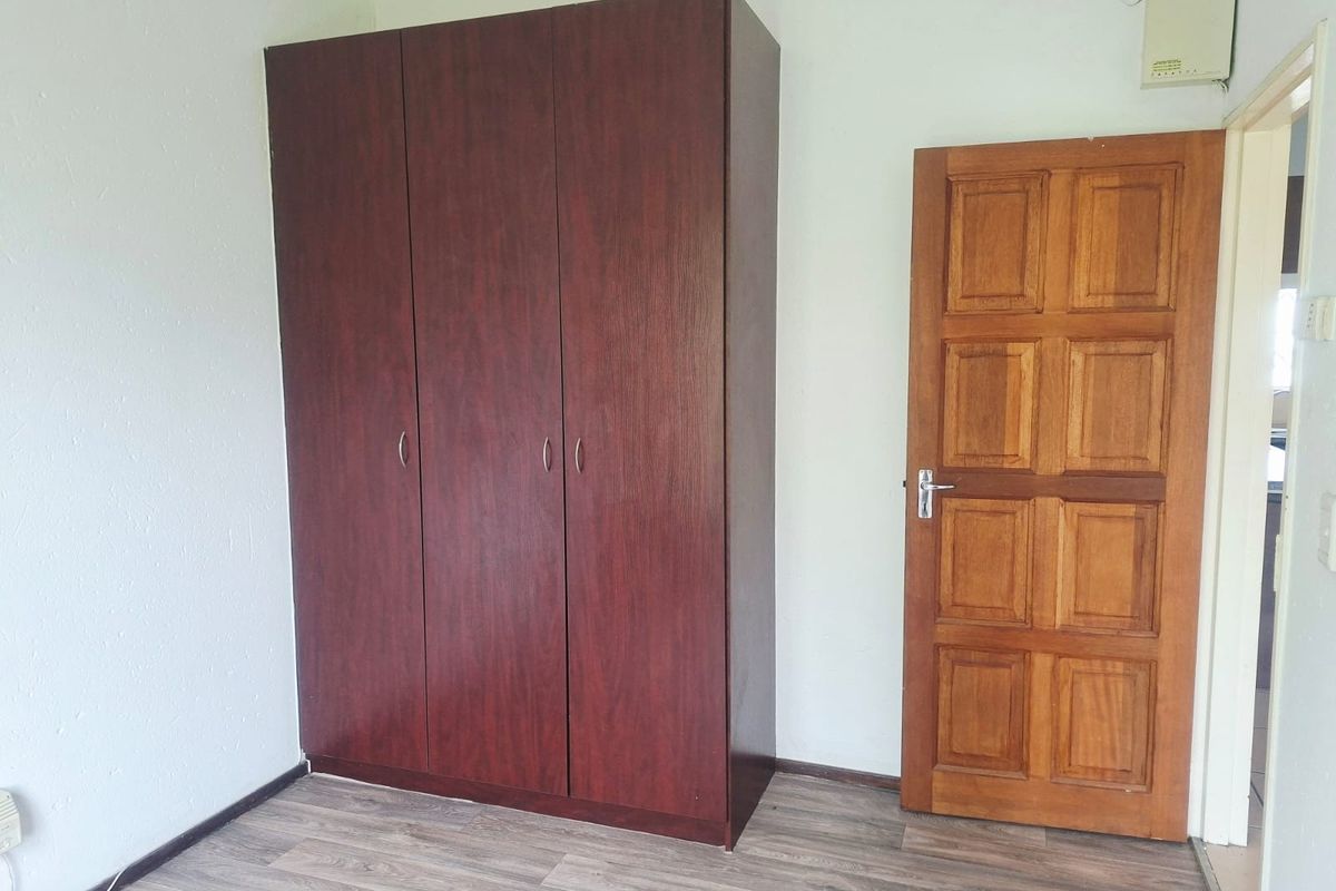 A bedroom featuring laminate flooring, a built-in wardrobe, and a solid timber panel door.