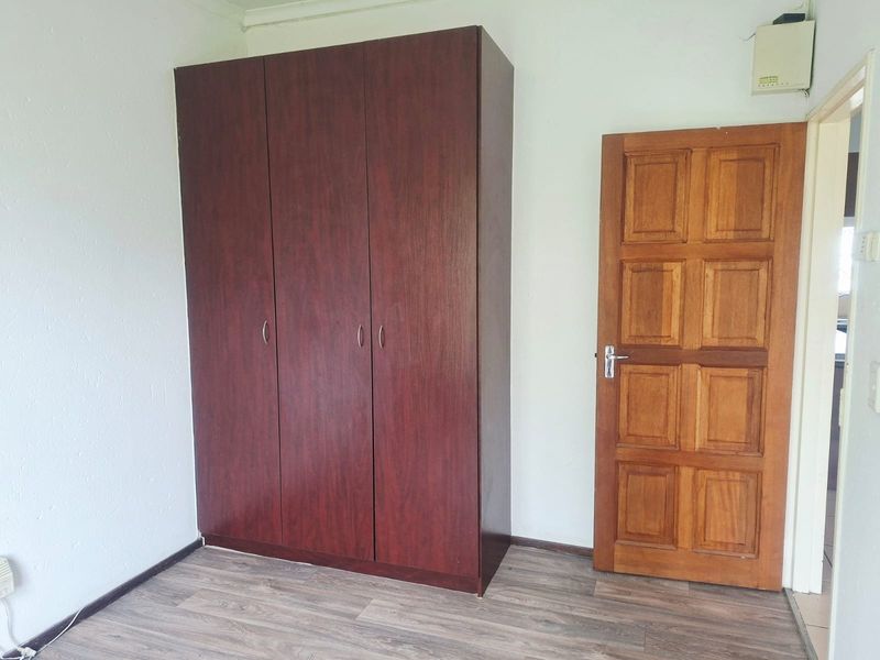 A bedroom featuring laminate flooring, a built-in wardrobe, and a solid timber panel door.