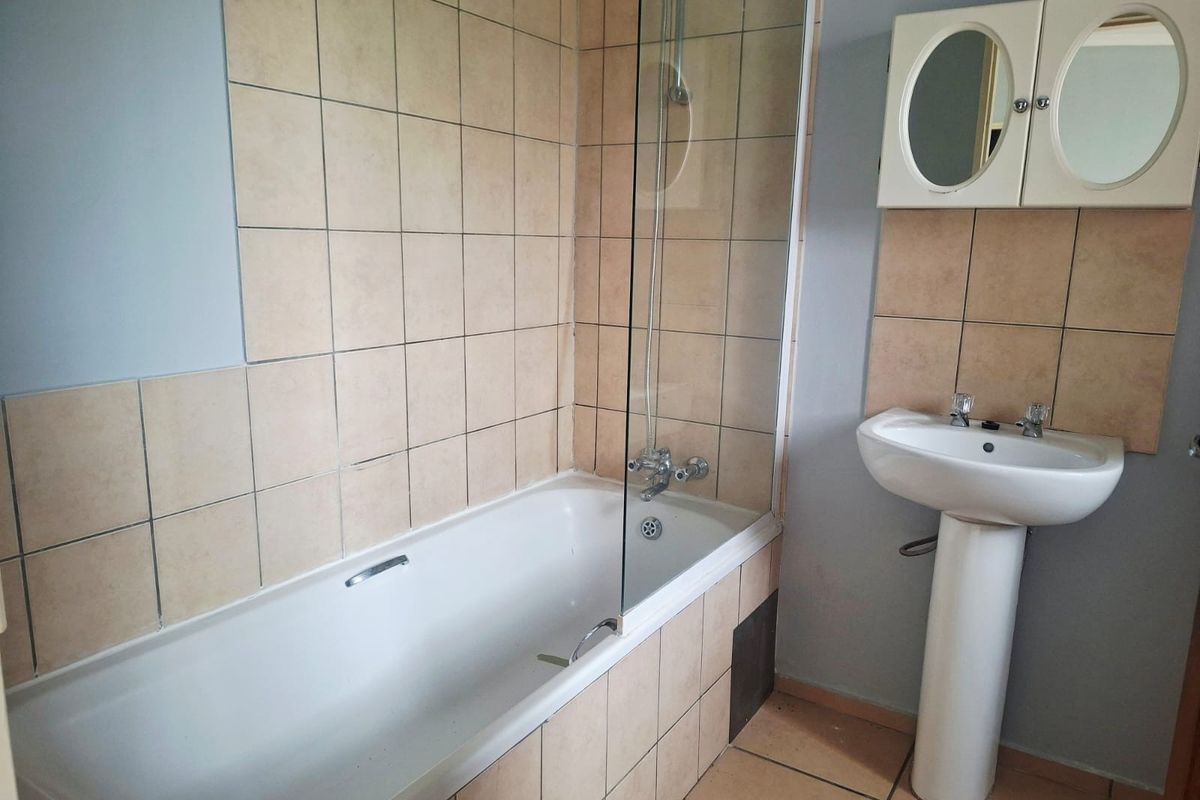 A functional bathroom featuring a pedestal basin, a bathtub with a glass shower screen, and neutral wall tiling.
