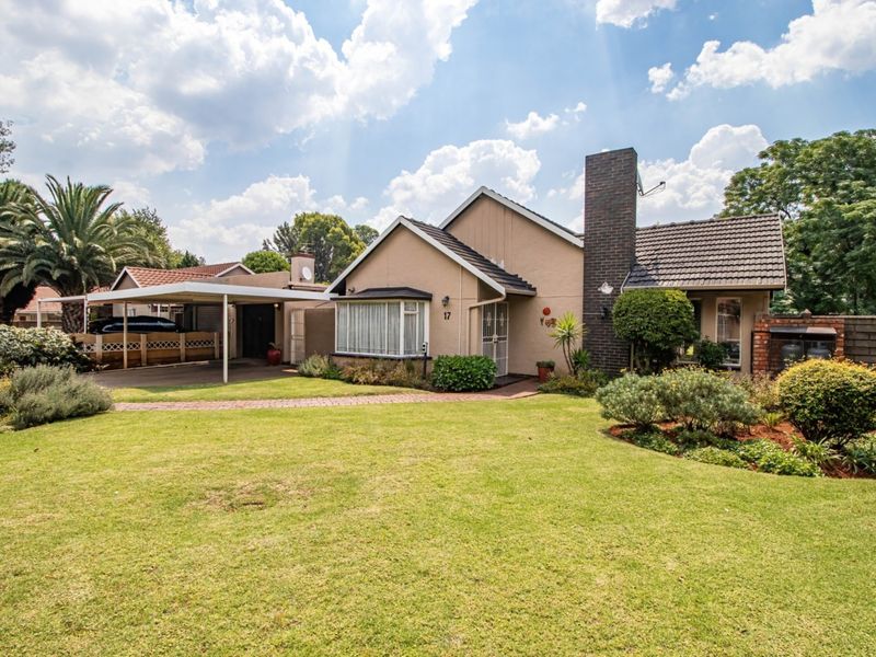 A well-maintained single-story house featuring a brick chimney, tiled roof, attached carport, and a neatly landscaped front garden with a paved walkway.