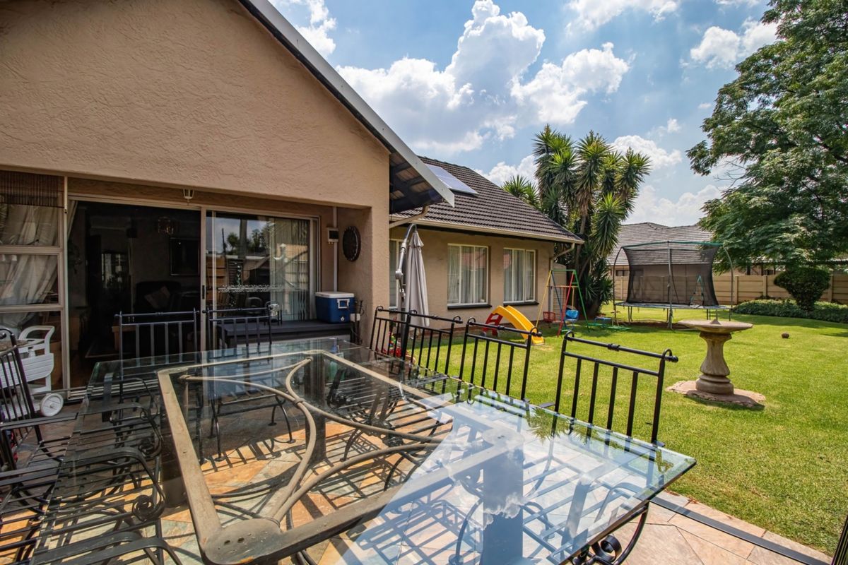 Rear view of the property featuring a covered tiled patio, sliding glass doors, and a well-maintained garden with a lawn.