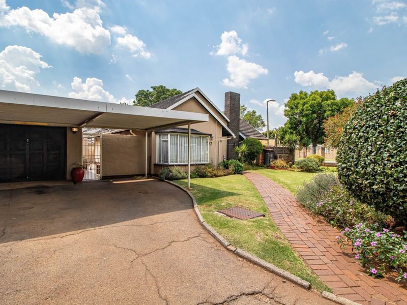 Front exterior view of the house featuring a paved driveway, attached carport, brick walkway, and established garden landscaping.