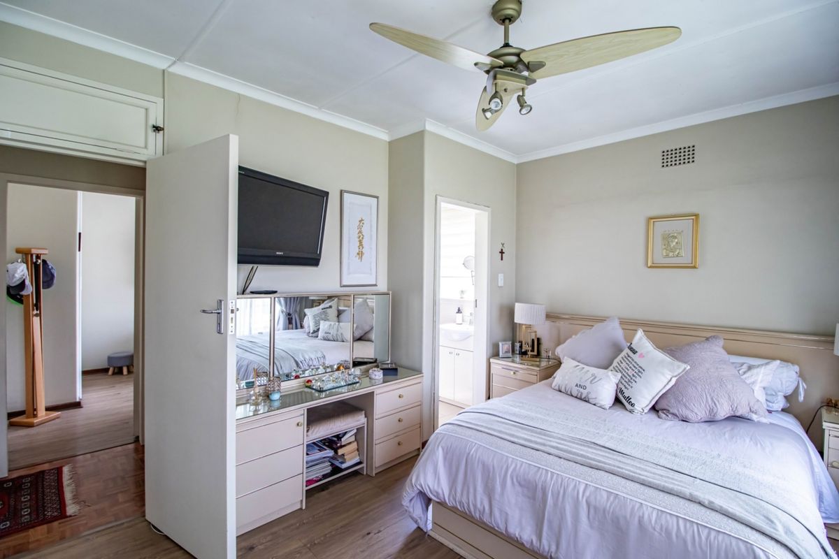 A bedroom featuring laminate flooring, a ceiling fan, and a built-in vanity unit with an integrated mirror.