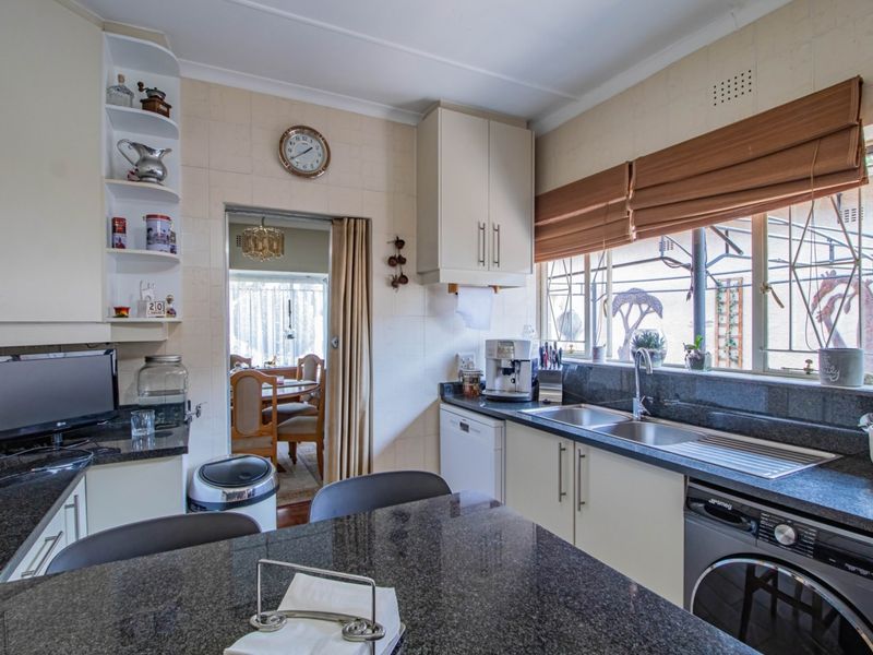 A functional kitchen featuring granite countertops, ample built-in cabinetry, a double stainless steel sink, and integrated laundry appliances with tiled wall finishes.