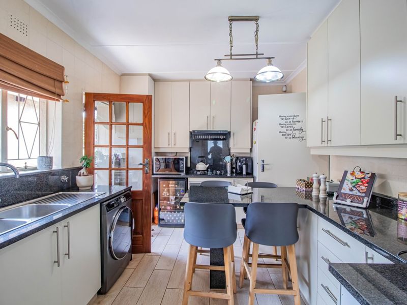 A well-appointed kitchen featuring granite countertops, ample cabinetry, a double basin sink, and a built-in wine cooler with integrated breakfast bar seating.
