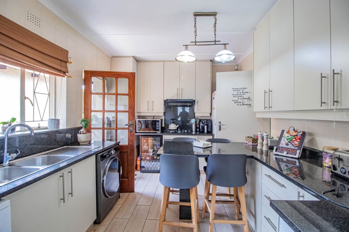 A well-appointed kitchen featuring granite countertops, ample cabinetry, a double basin sink, and a built-in wine cooler with integrated breakfast bar seating.