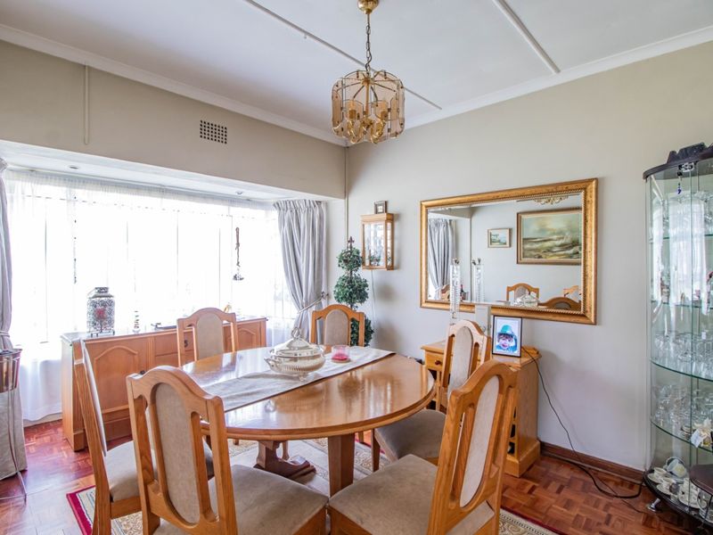 A traditional dining room featuring classic parquet flooring, a large bay window providing natural light, and a decorative ceiling fixture.