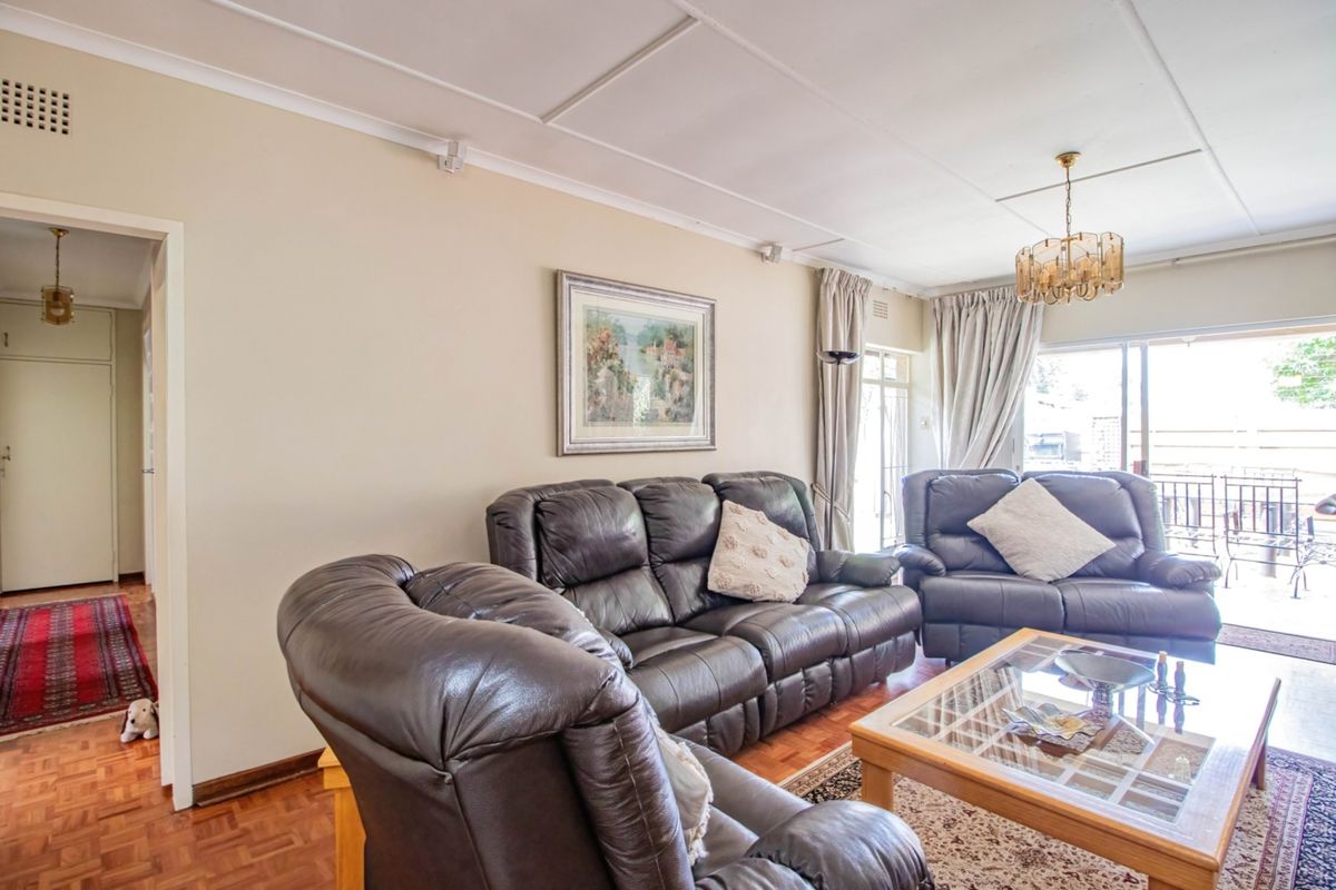 A spacious living room featuring classic parquet flooring, large sliding glass doors providing natural light, and access to an outdoor patio area.
